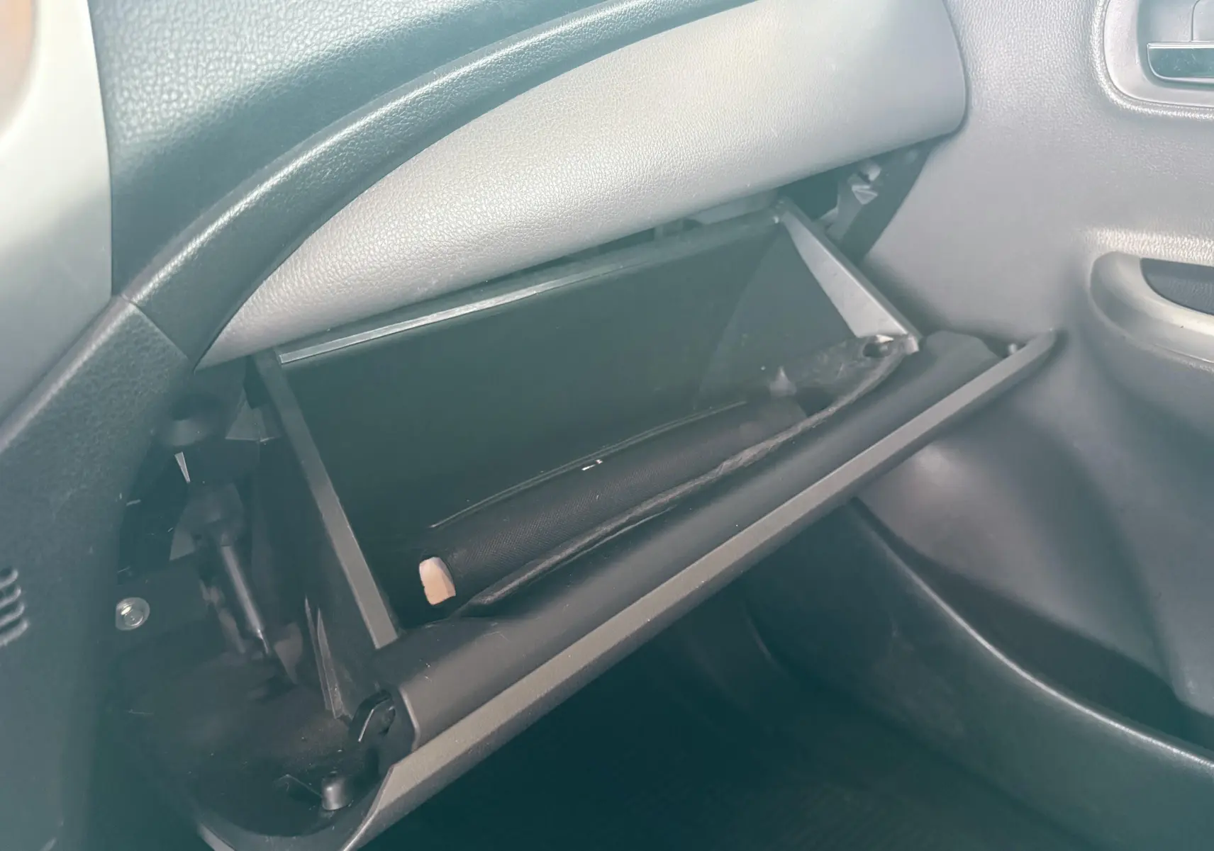 Gros plan sur la boîte à gants ouverte côté passager du Mitsubishi L200 blanc, montrant un rangement intérieur vide.