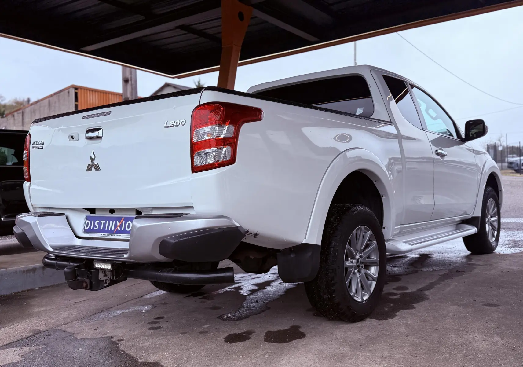 Vue 3/4 arrière droite du pick-up Mitsubishi L200 Club Cab blanc, avec hayon fermé et pare-chocs arrière gris.