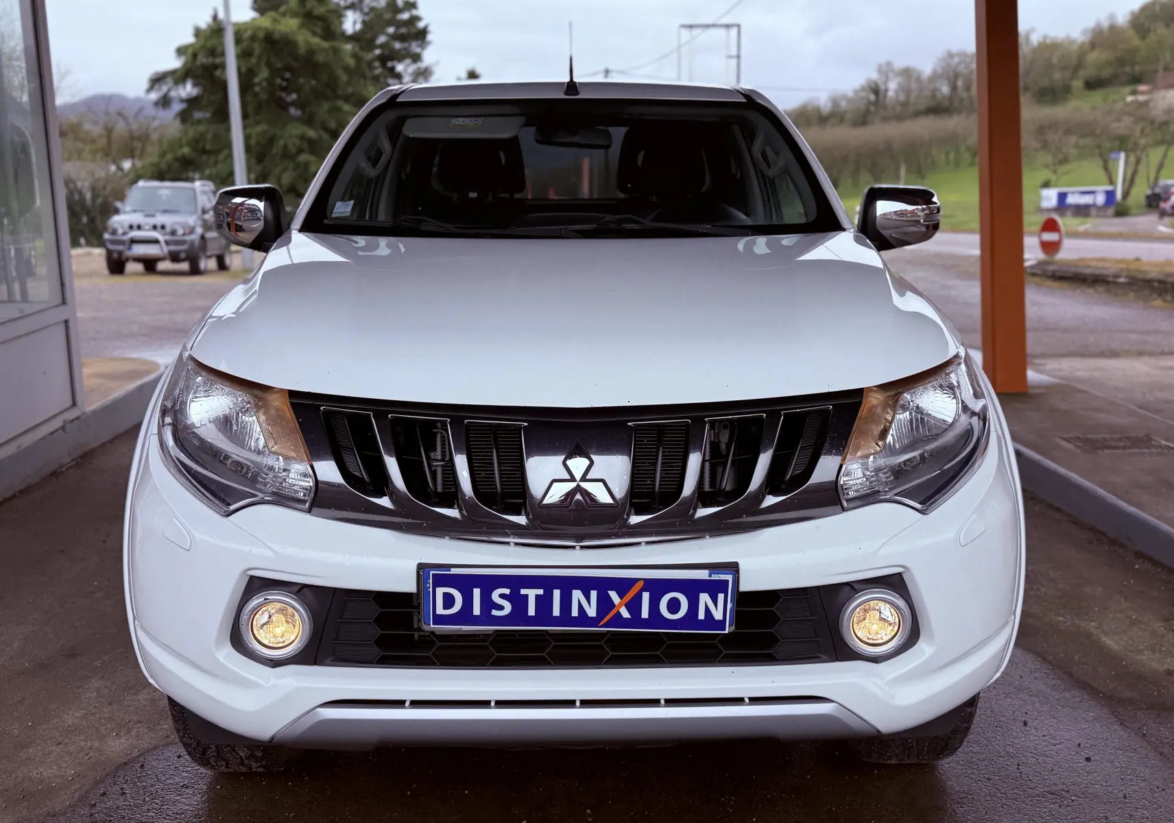 Vue frontale d’un Mitsubishi L200 Club Cab blanc de 2017 avec phares et antibrouillards allumés, calandre noire distinctive.