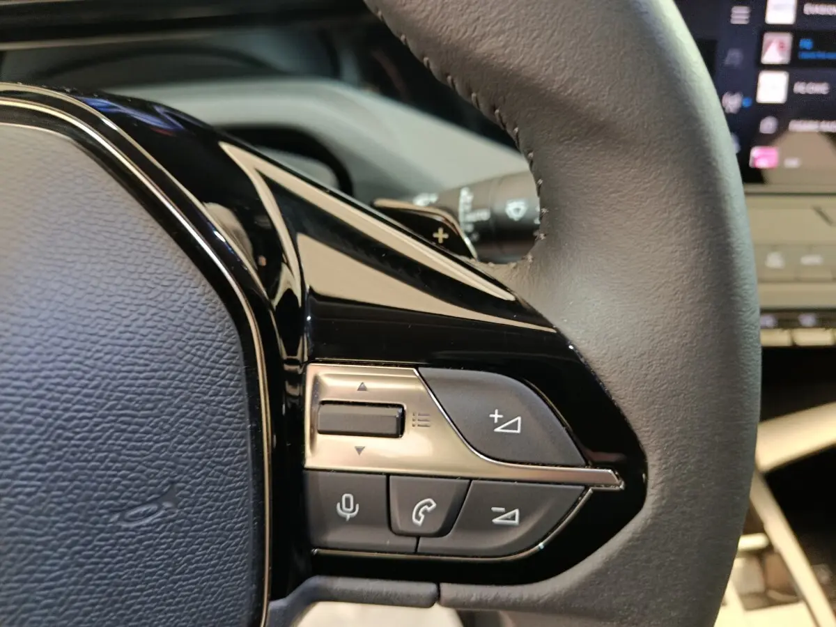 Gros plan sur les commandes multifonctions côté gauche du volant cuir d’une Peugeot 308 blanche, intérieur moderne.