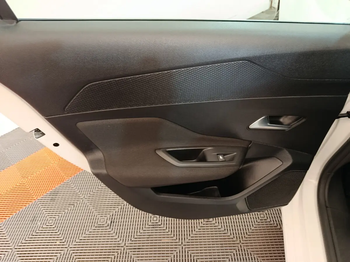 Vue intérieure de la porte côté droit de la Peugeot 308 blanche, avec poignée argentée et commande de lève-vitre noir.