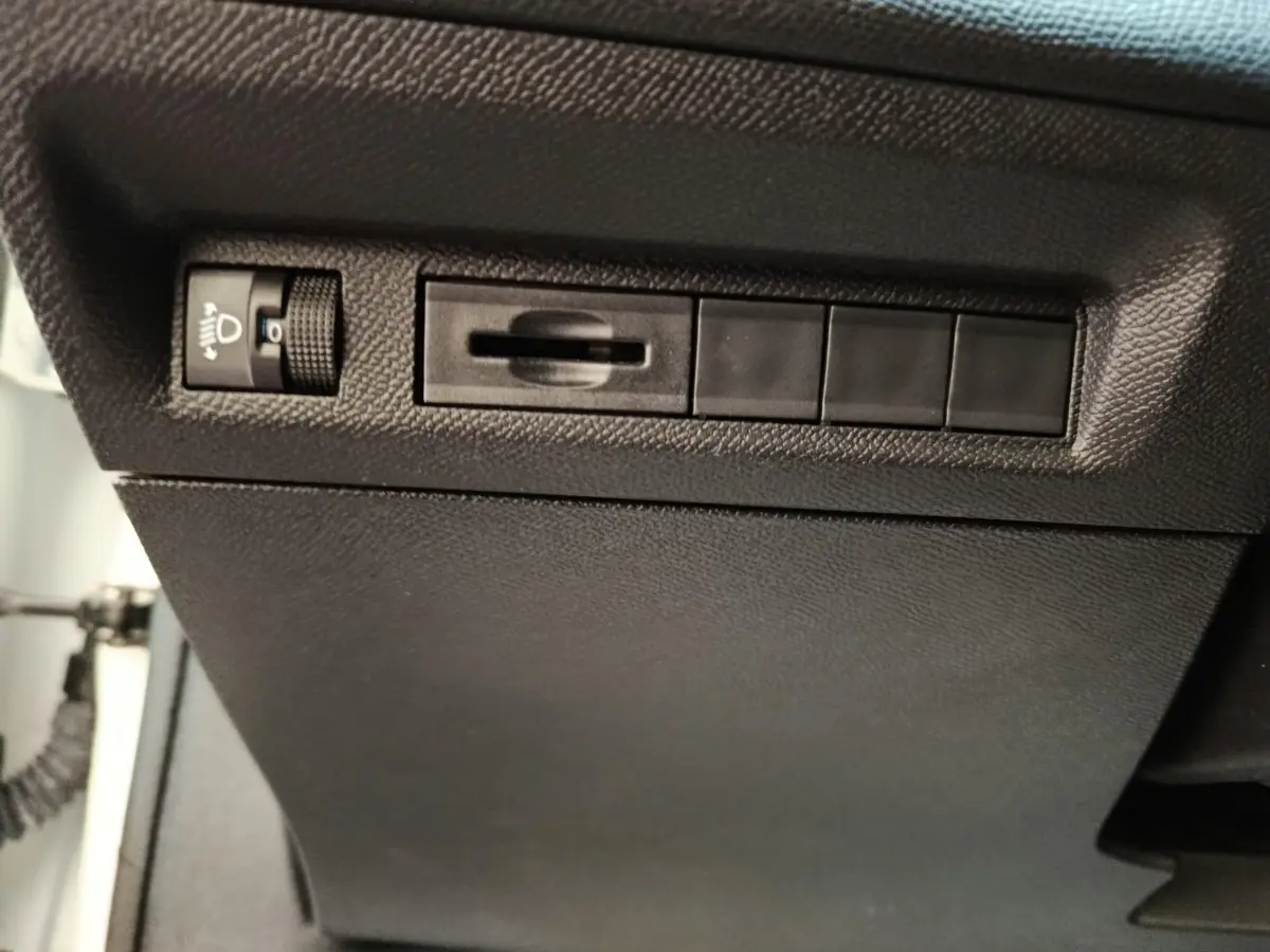 Détail intérieur côté conducteur de la Peugeot 308 blanche 2022 montrant les commandes de réglage des phares.