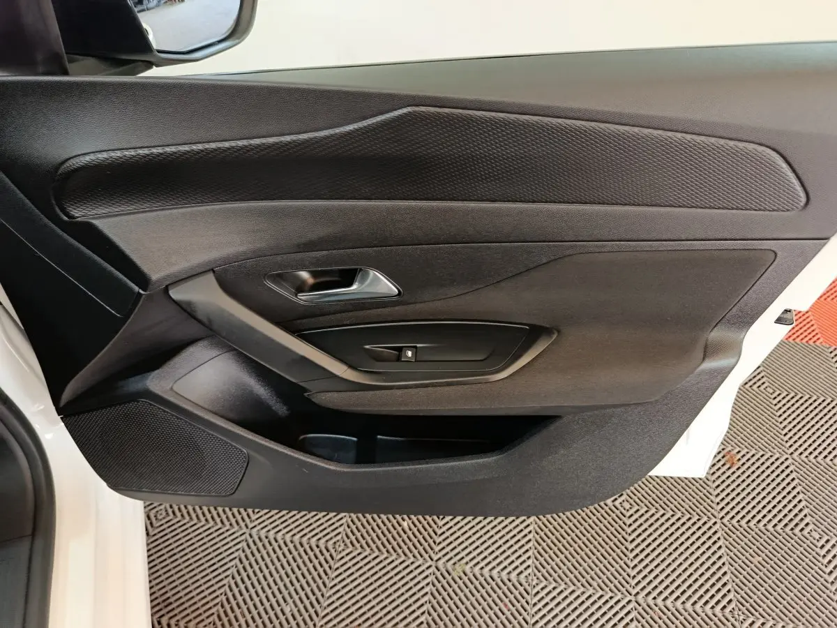 Vue rapprochée de la porte avant gauche noire d’une Peugeot 308 blanche, mettant en valeur la poignée et les commandes de fenêtre.