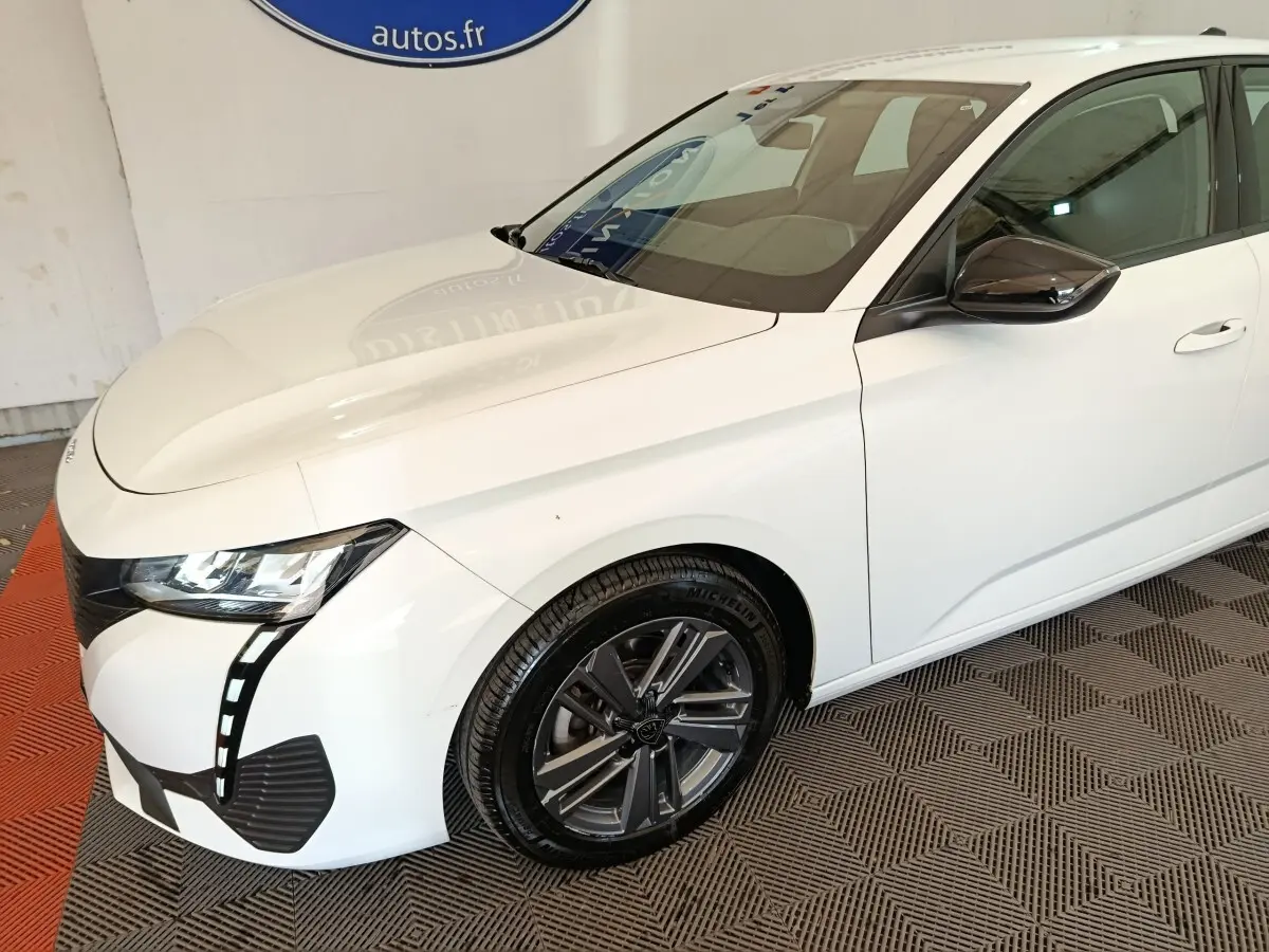 Vue 3/4 avant droit d'une Peugeot 308 blanche avec phares LED et jantes alliage foncé.