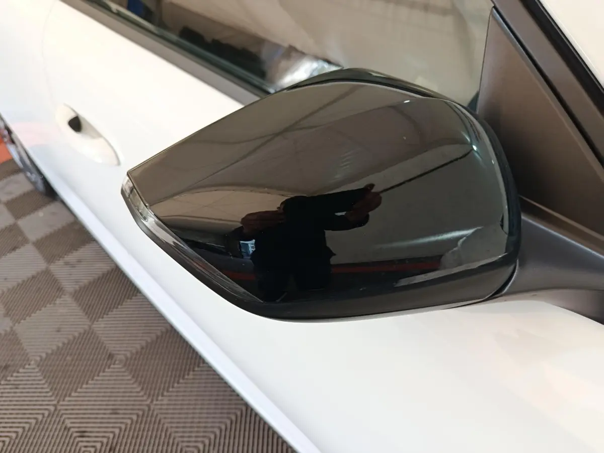 Rétroviseur noir brillant côté conducteur d'une Peugeot 308 blanche vue de près en intérieur.
