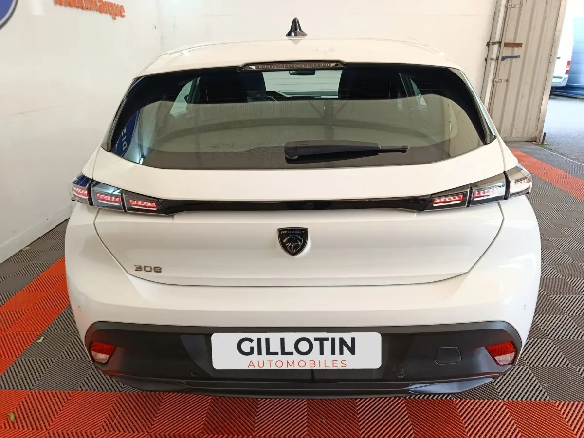 Vue arrière d'une Peugeot 308 blanche de 2022 avec feux LED et logo lion distinctif au centre du hayon.
