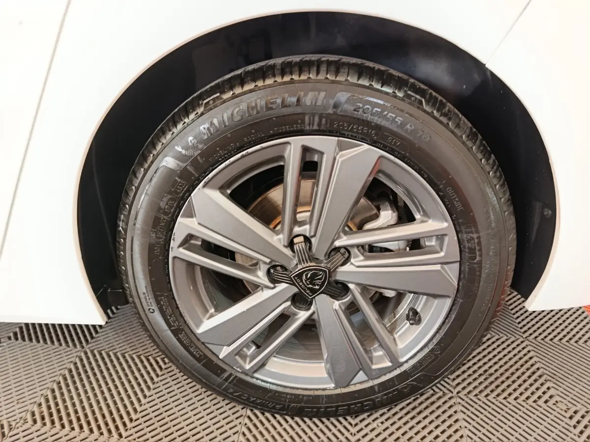 Gros plan sur la roue avant droite d'une Peugeot 308 blanche, jante alliage gris avec logo Lion central.