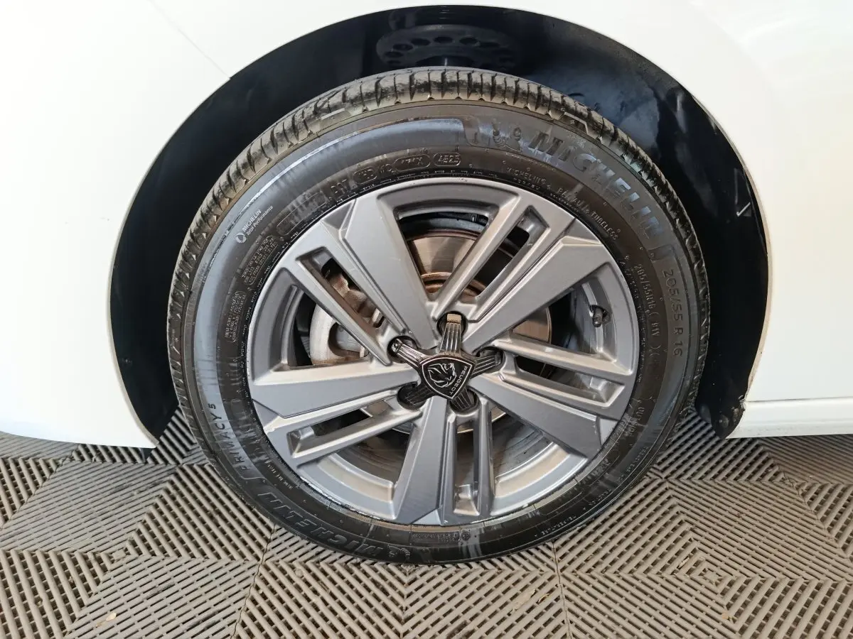 Gros plan sur la roue avant droite d’une Peugeot 308 blanche avec jante alliage gris et logo lion central.