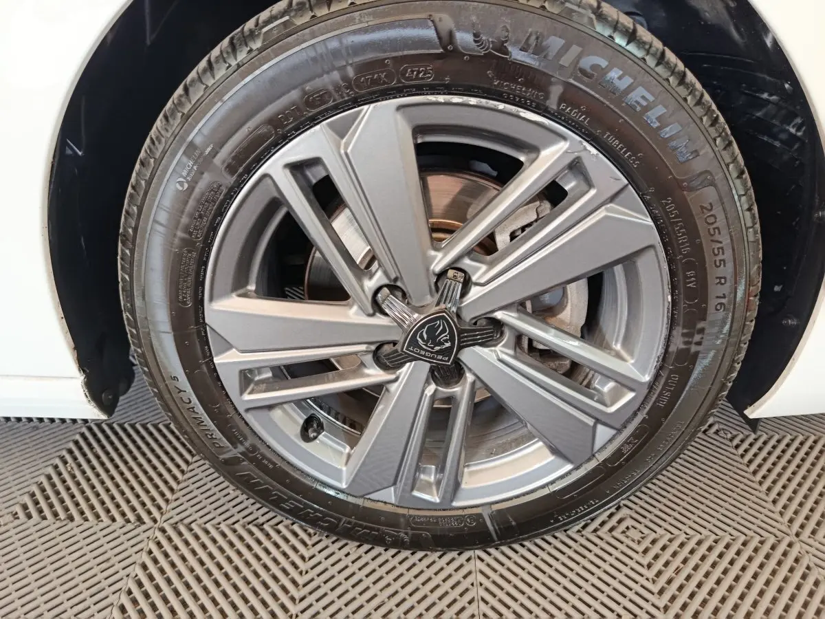 Gros plan sur la roue avant droite d'une Peugeot 308 blanche, mettant en valeur la jante alliage grise au design moderne.