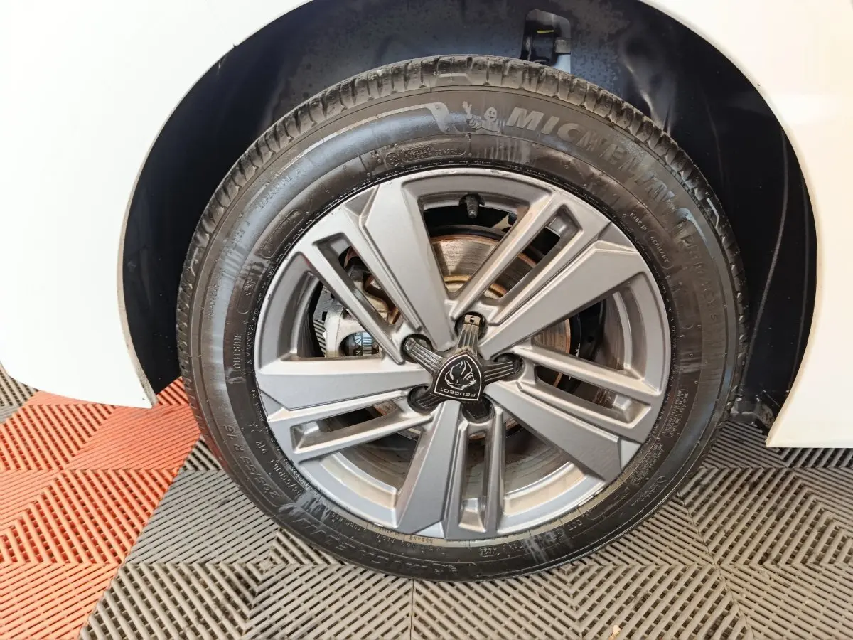 Gros plan sur la roue avant droite de la Peugeot 308 blanche, mettant en valeur la jante alliage grise au design moderne.