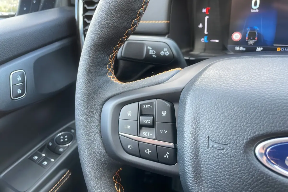 Gros plan sur le volant cuir noir avec surpiqûres orange et commandes multifonctions du Ford Ranger Wildtrak 2025.