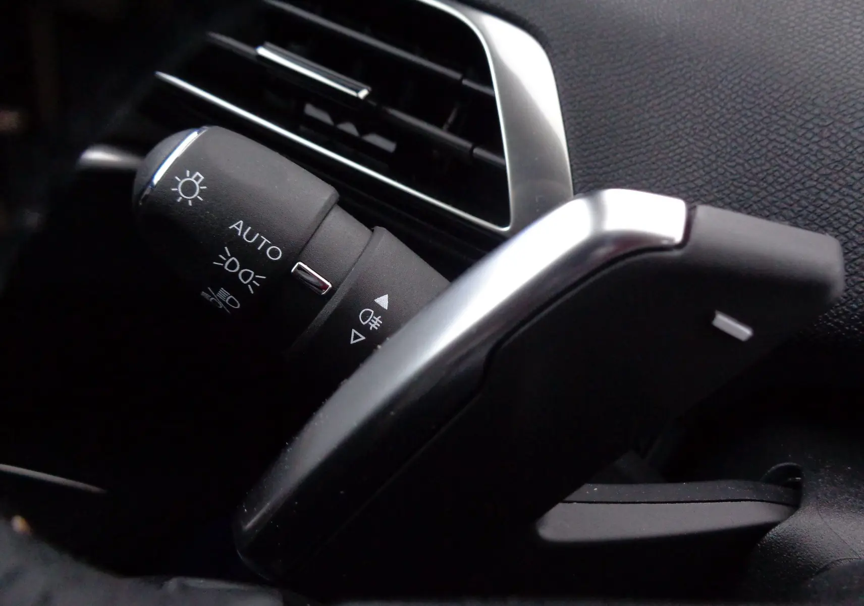 Gros plan sur la commande des phares et la palette de changement de vitesse côté gauche dans l'habitacle noir du Peugeot 3008 2023.