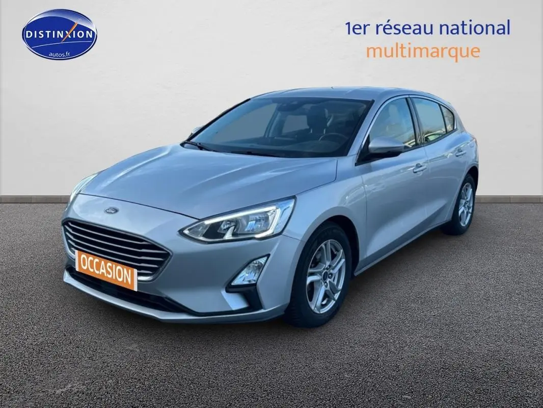 Ford Focus gris clair vue 3/4 avant droit, avec jantes alliage 16 pouces et feux allumés diurnes.