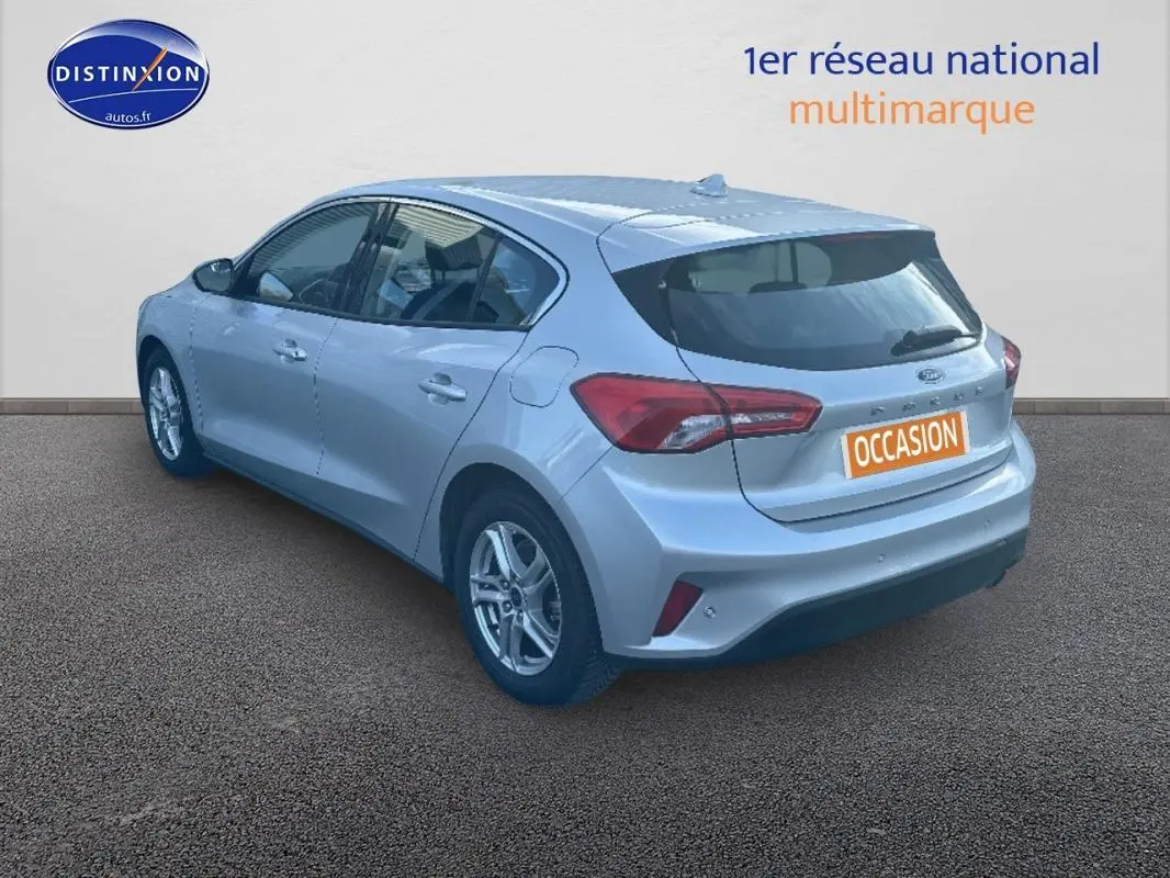 Ford Focus gris clair vue 3/4 arrière droit, avec jantes alliage 16 pouces et feux arrière distinctifs.