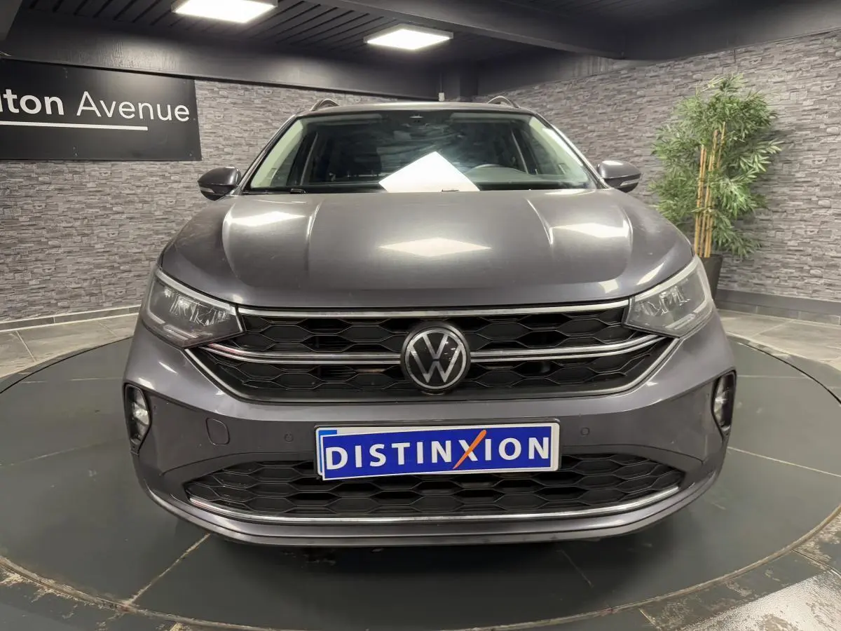 Vue frontale d'un Volkswagen Taigo gris Ascot avec calandre noire et logo VW centré, en showroom intérieur.