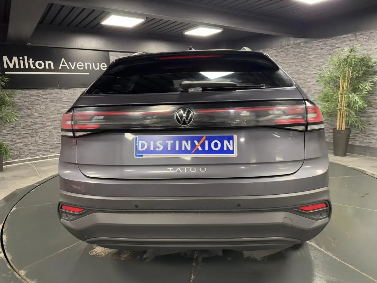 Vue arrière d'un Volkswagen Taigo gris Ascot avec feux arrière LED et logo central lumineux dans un showroom.