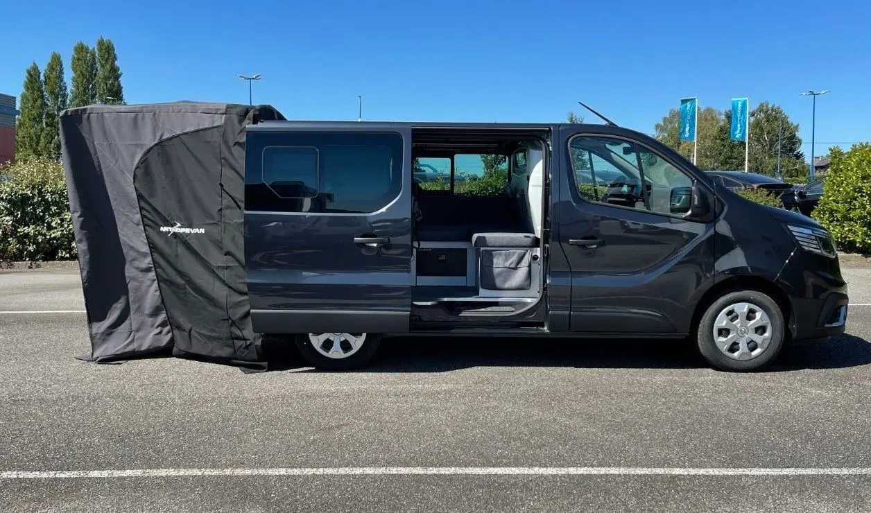 Profil côté droit du Renault Trafic Fourgon gris Comète 2022 avec porte coulissante ouverte et tente d’auvent déployée à l’arrière.