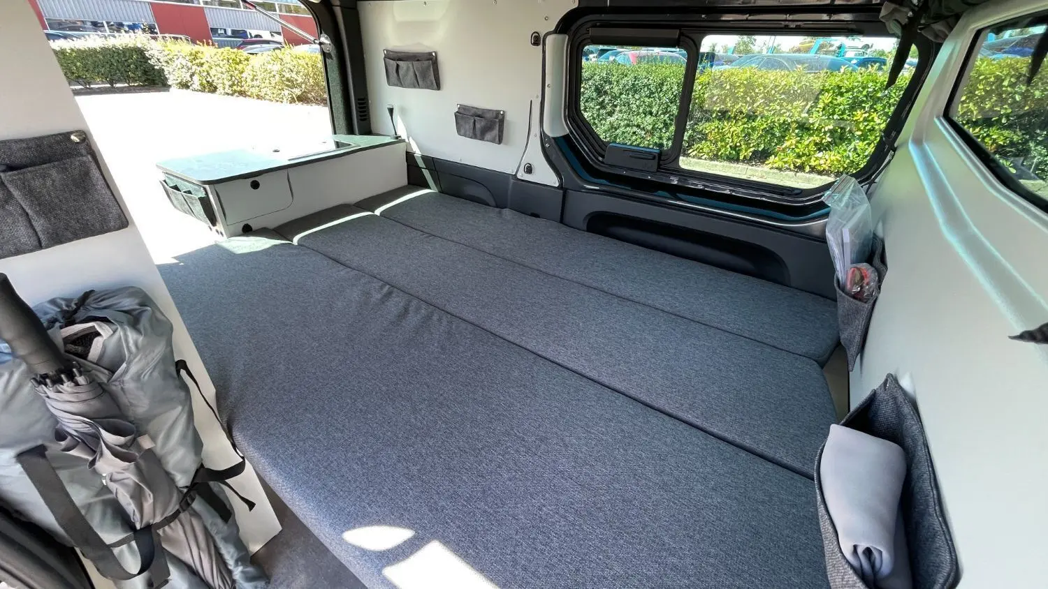 Intérieur du Renault Trafic Fourgon gris Comète, vue latérale droite montrant le lit adulte déplié et rangements muraux.