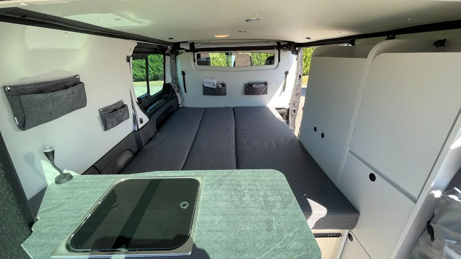 Intérieur du Renault Trafic Fourgon gris Comète, vue arrière montrant le lit double et les rangements blancs intégrés.