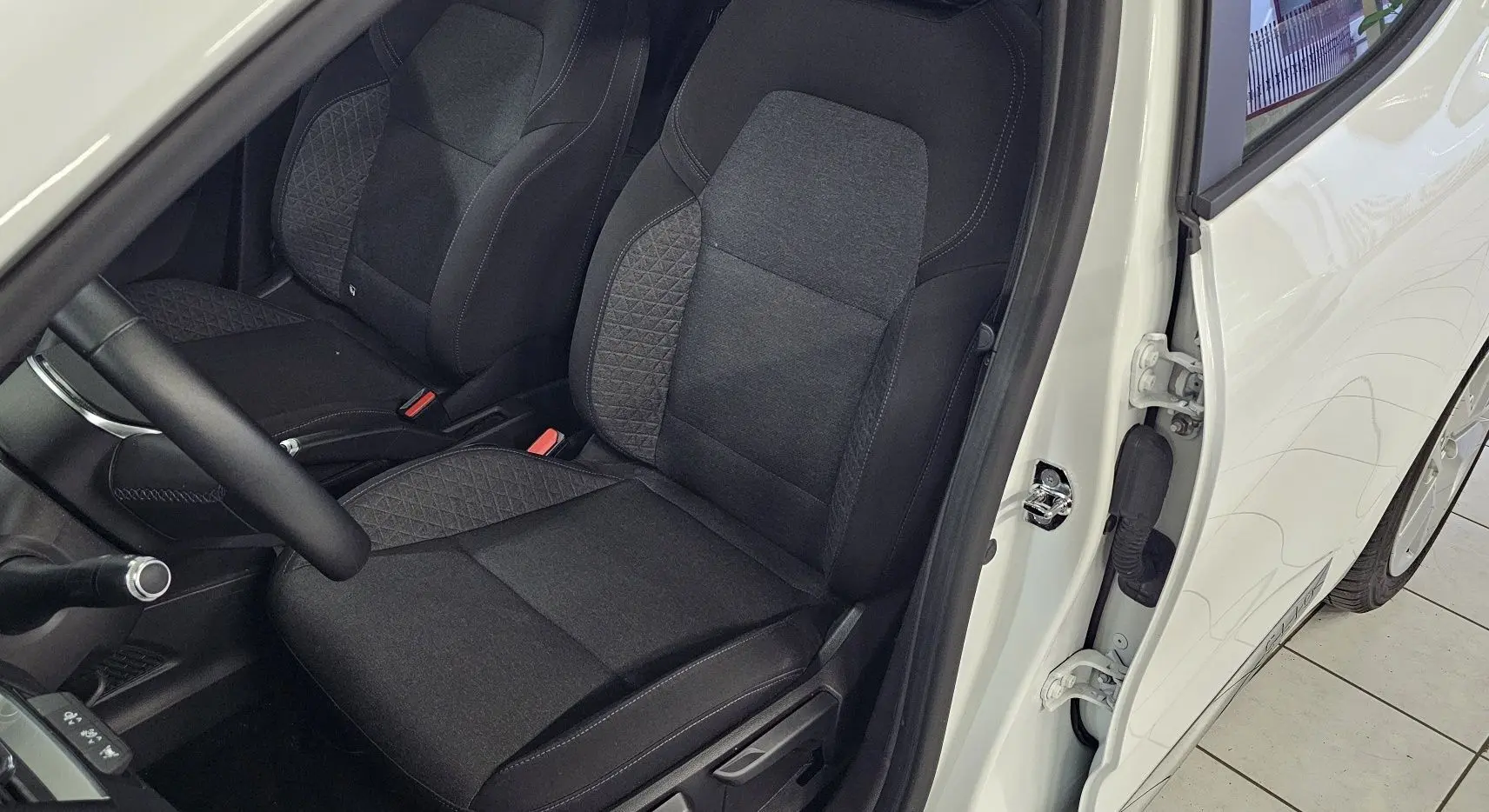 Vue intérieure côté conducteur de la Renault Clio blanche glacier 2020, avec sièges tissu gris et noir détaillés.