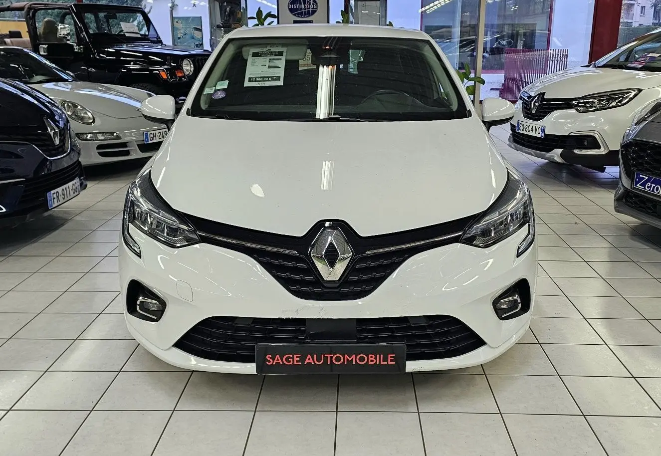 Vue frontale d'une Renault Clio blanche glacier 2020 en showroom avec calandre noire et phares LED.