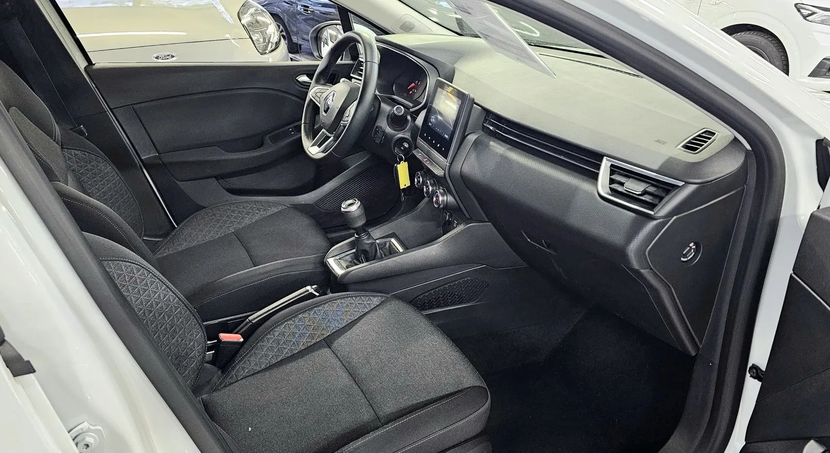 Intérieur côté conducteur d'une Renault Clio blanche glacier 2020 avec sièges noirs et tableau de bord moderne.