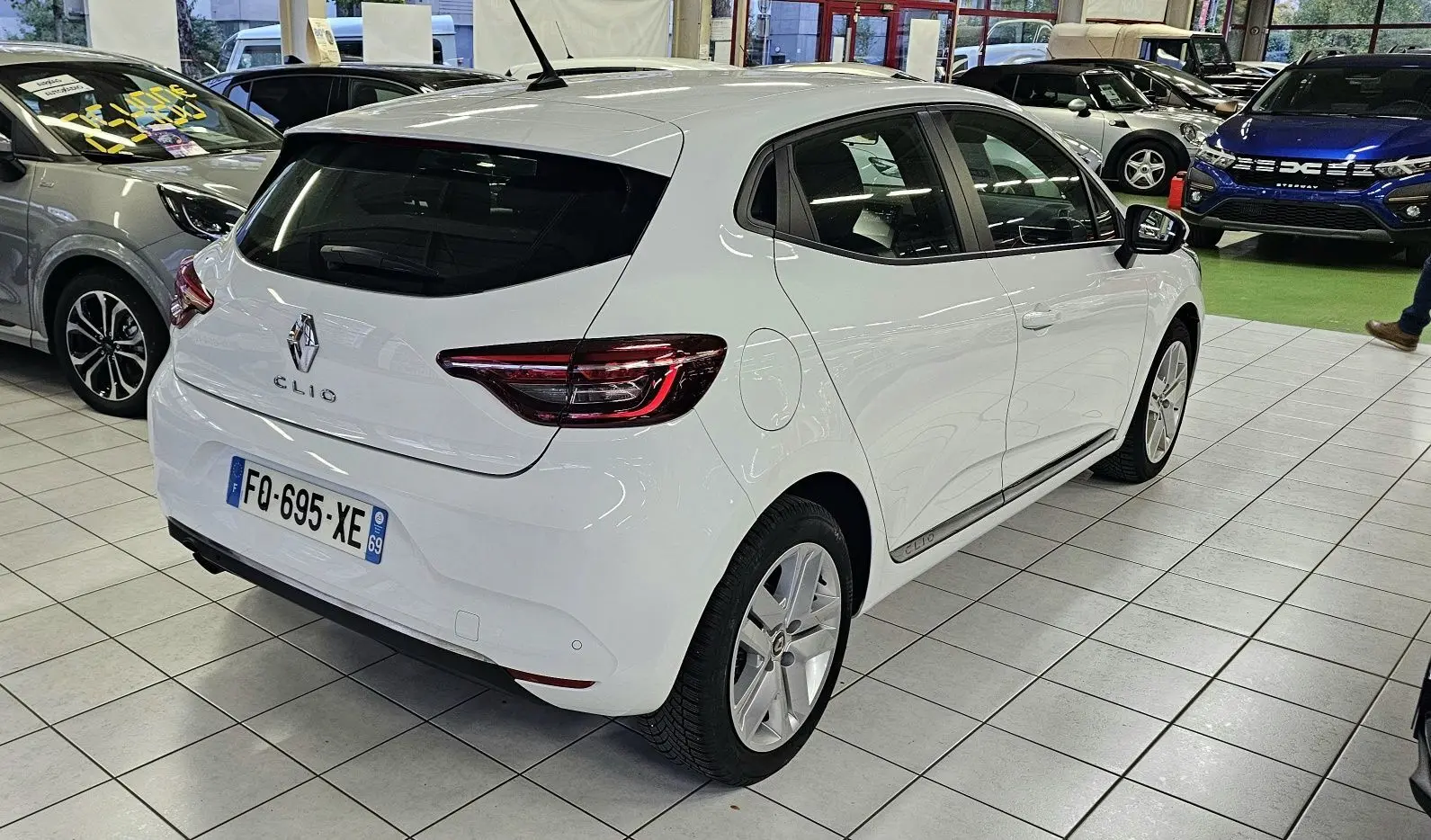 Vue 3/4 arrière droite d'une Renault Clio blanche Glacier en showroom avec jantes alliage et feux LED distinctifs.