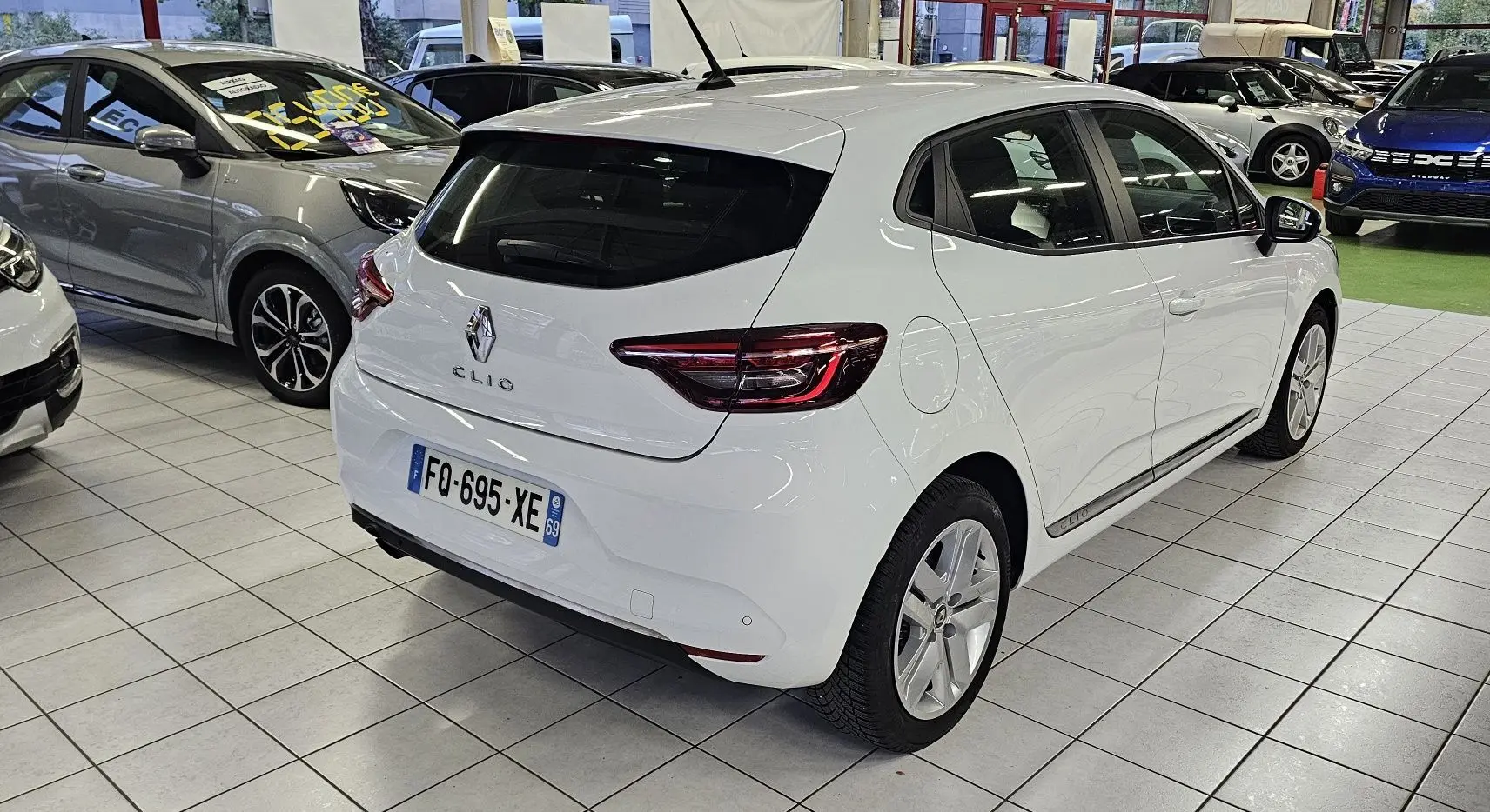 Renault Clio blanc glacier vue 3/4 arrière droit dans un showroom, avec feux arrière LED distinctifs.