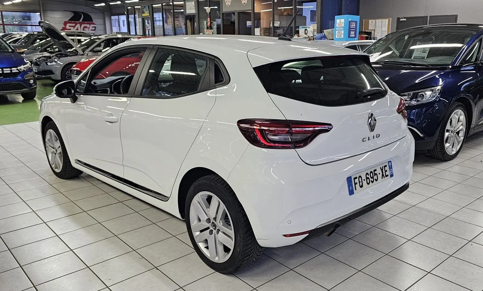 Vue 3/4 arrière droite d'une Renault Clio blanche Glacier 2020 en intérieur, avec feux arrière LED et cinq portes visibles.