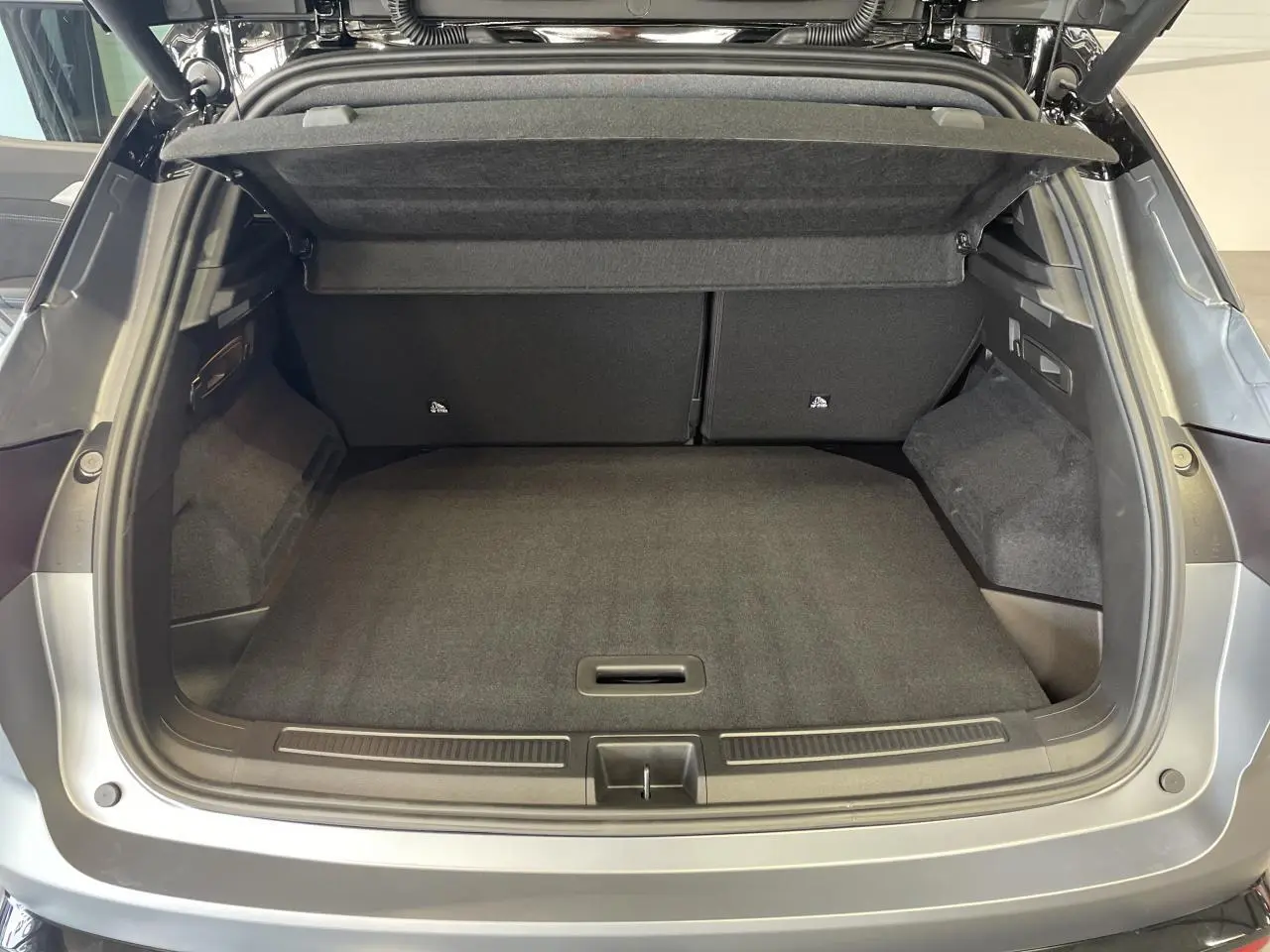 Coffre ouvert vu de l'arrière d'un Renault Austral gris satin mat avec intérieur de coffre noir et cache-bagages relevé.