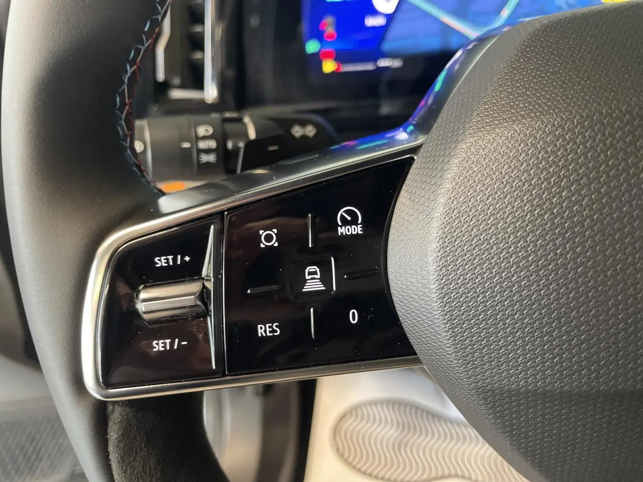 Gros plan sur les commandes gauche du volant textile Alcantara du Renault Austral gris satin mat, avec affichage numérique en arrière-plan.