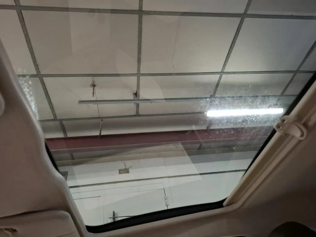 Vue intérieure du toit ouvrant panoramique d'une Fiat 500 Dolcevita gris électroclash, éclairage de garage visible.