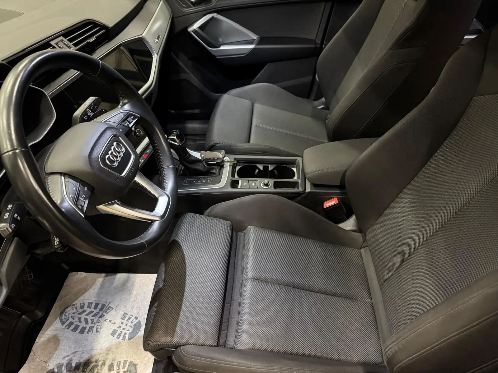 Vue intérieure côté conducteur de l'Audi Q3 Business 2019 avec sellerie tissu gris et volant multifonction.