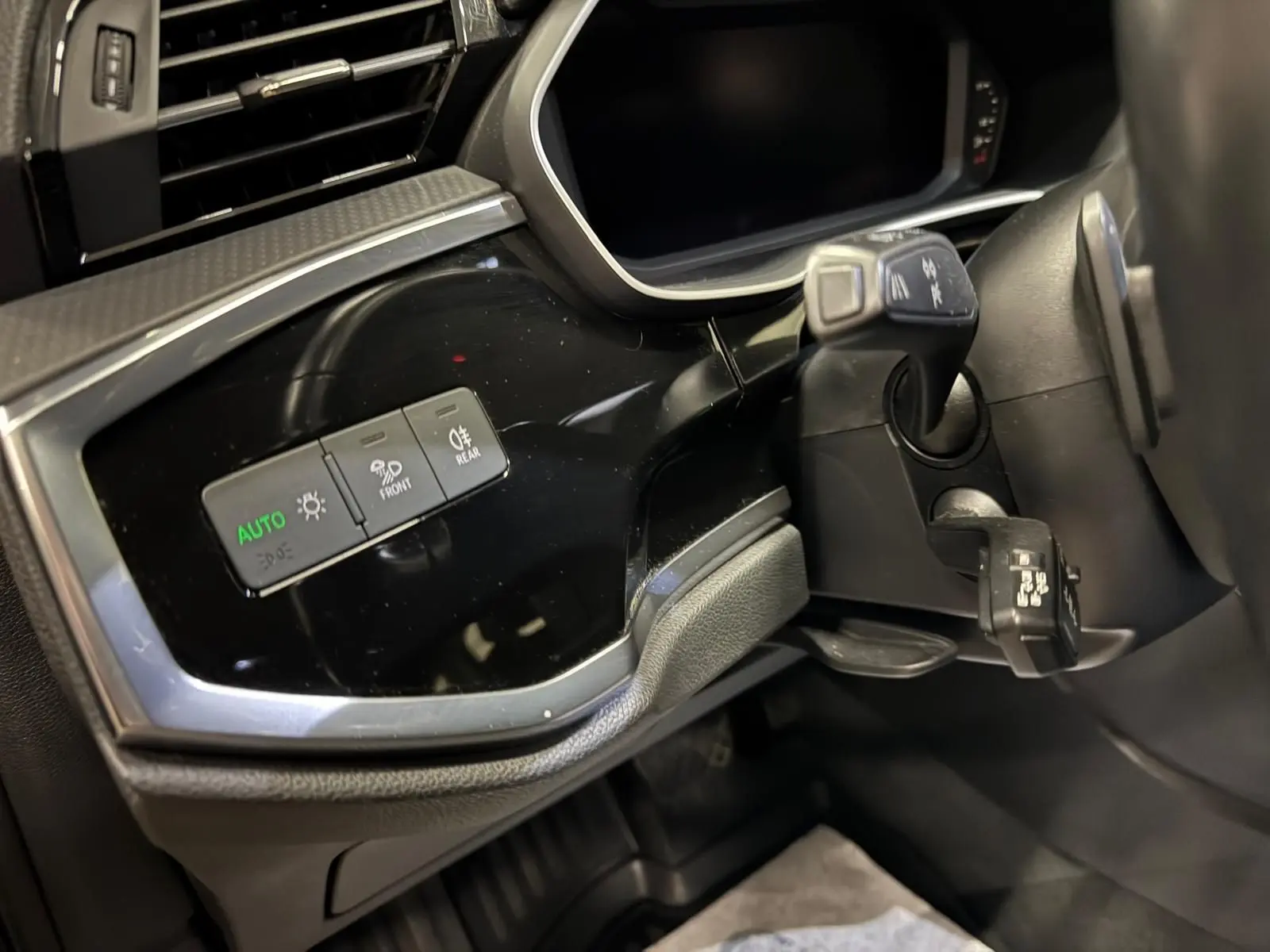 Détail du tableau de bord côté gauche de l'Audi Q3 Business gris, avec commandes d'éclairage et inserts noir brillant.