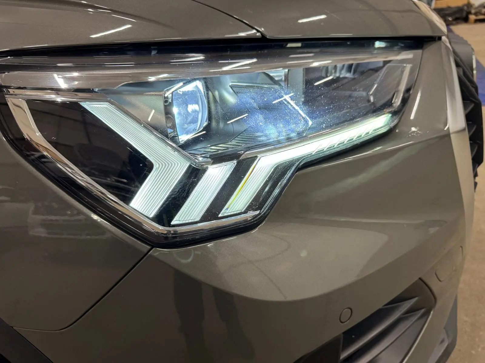 Gros plan sur le phare avant droit LED dynamique d’un Audi Q3 Business gris, soulignant ses lignes modernes et précises.