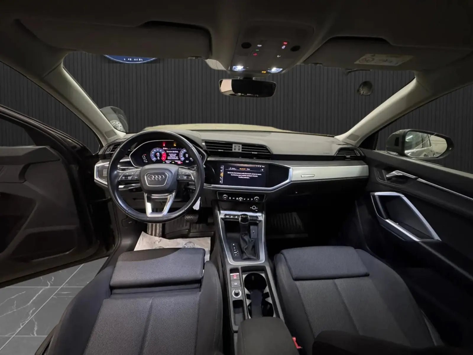Vue intérieure avant de l'Audi Q3 Business 2019, avec tableau de bord moderne et sellerie tissu gris foncé.