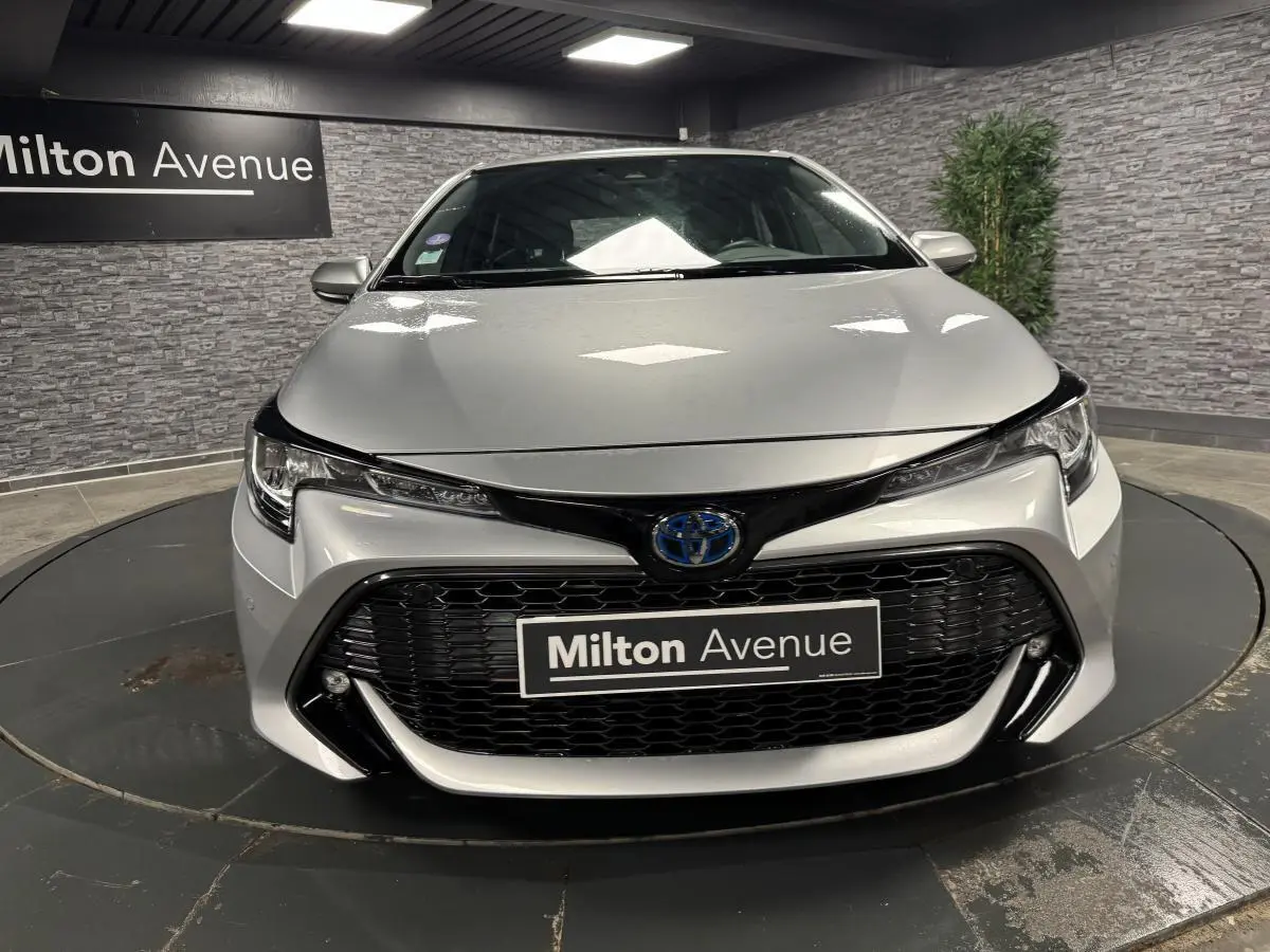 Vue frontale d'une Toyota Corolla hybride gris métallisé avec calandre noire et phares LED dans un showroom.