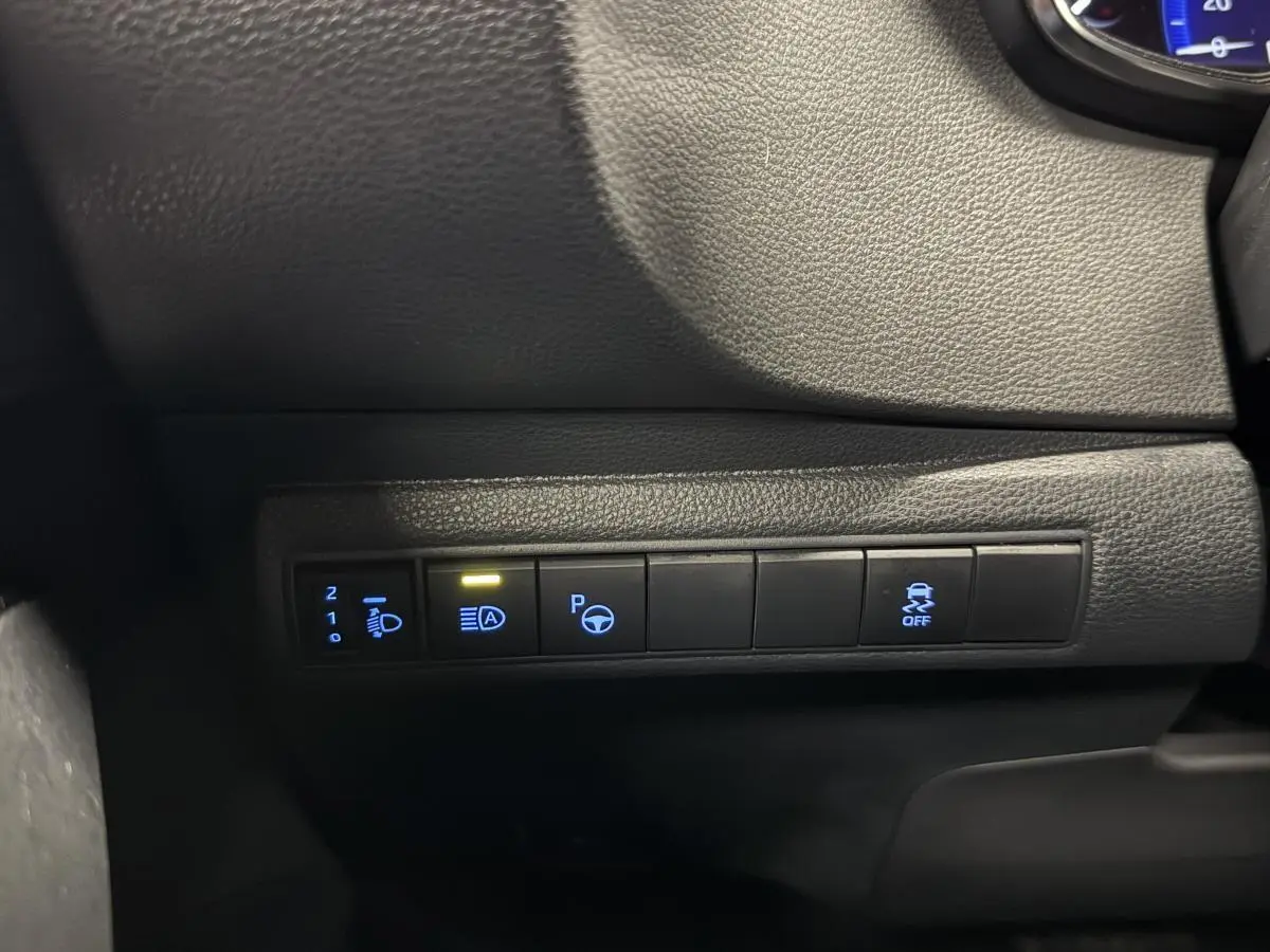 Gros plan sur les commandes de bord noires éclairées en bleu et jaune dans l'habitacle de la Toyota Corolla hybride gris 2022.
