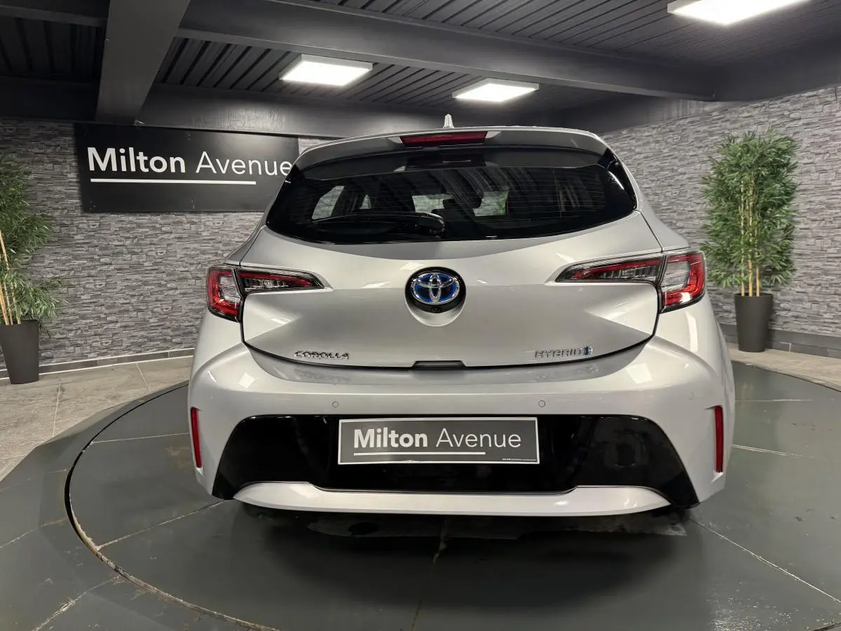 Vue arrière d'une Toyota Corolla hybride gris métallisé avec logo Toyota et feux arrière LED dans un showroom.