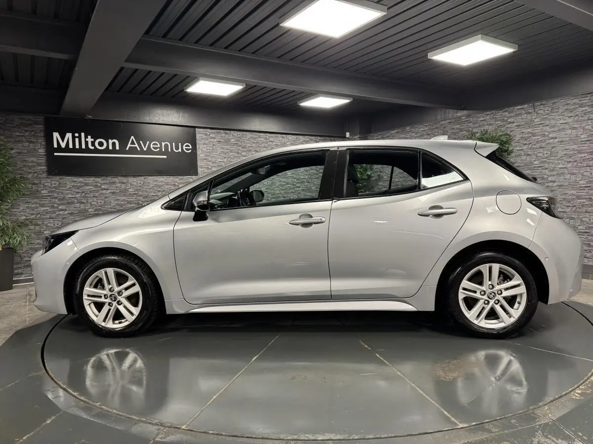 Profil côté gauche d'une Toyota Corolla hybride gris métallisé, avec jantes alliage et poignées couleur carrosserie.