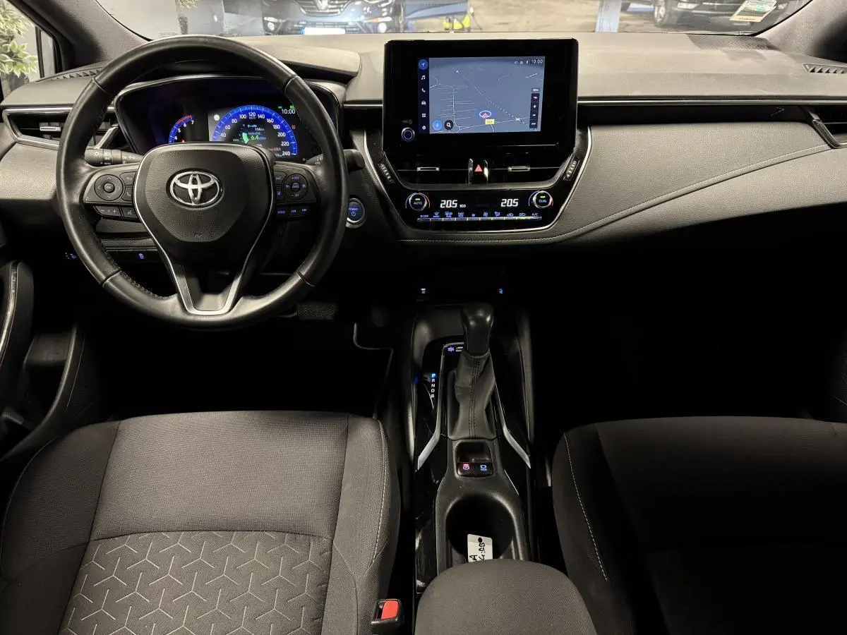 Intérieur de la Toyota Corolla Hybride 2022 vu de face, tableau de bord noir avec écran tactile et volant cuir multifonction.