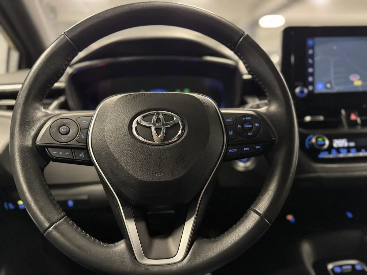Volant cuir noir Toyota Corolla Hybride 2022 vu de face, avec commandes multifonctions et écran tactile en arrière-plan.