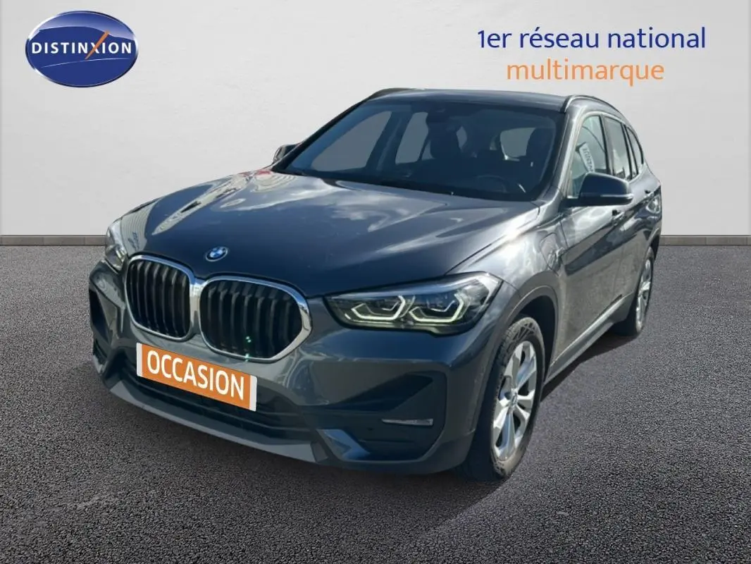BMW X1 gris foncé vue 3/4 avant droit, avec calandre double haricot et phares LED allumés.