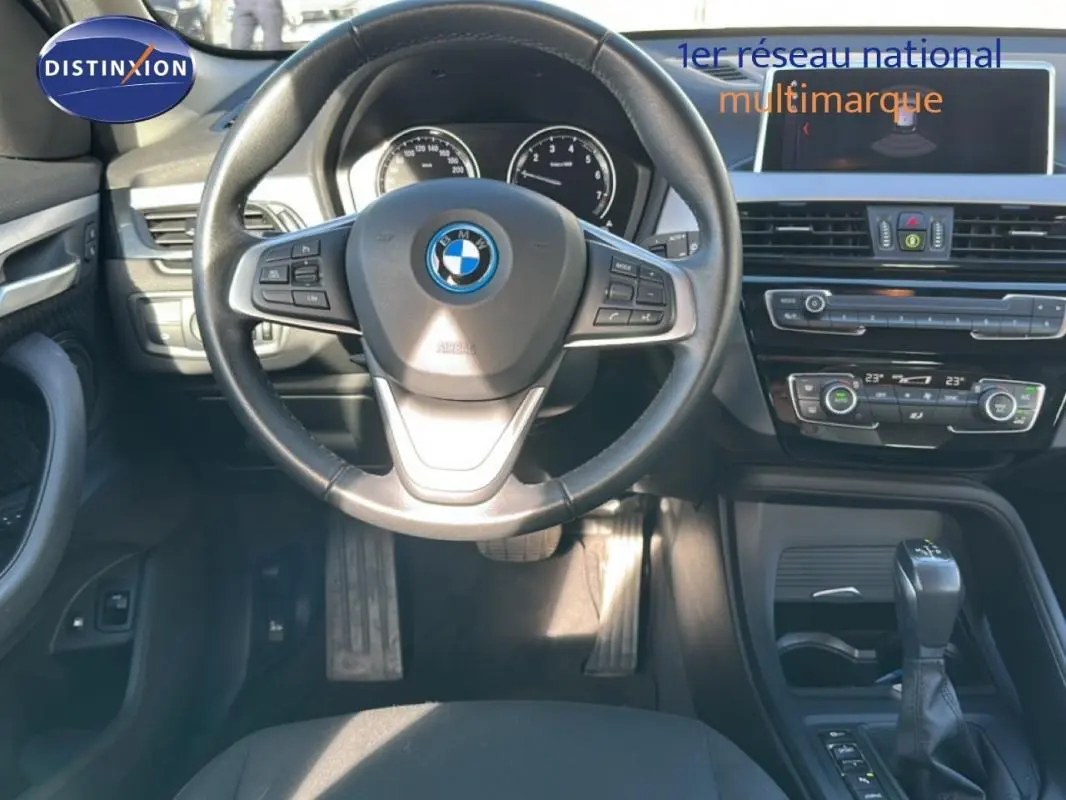 Vue intérieure centrée sur le volant sport et la console centrale d'une BMW X1 gris foncé avec écran GPS et boîte auto.