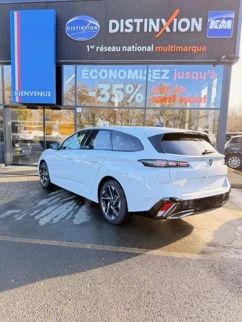 Vue 3/4 arrière droite d'une Peugeot 308 Hybrid blanche stationnée devant une vitrine avec enseigne Distinxion.