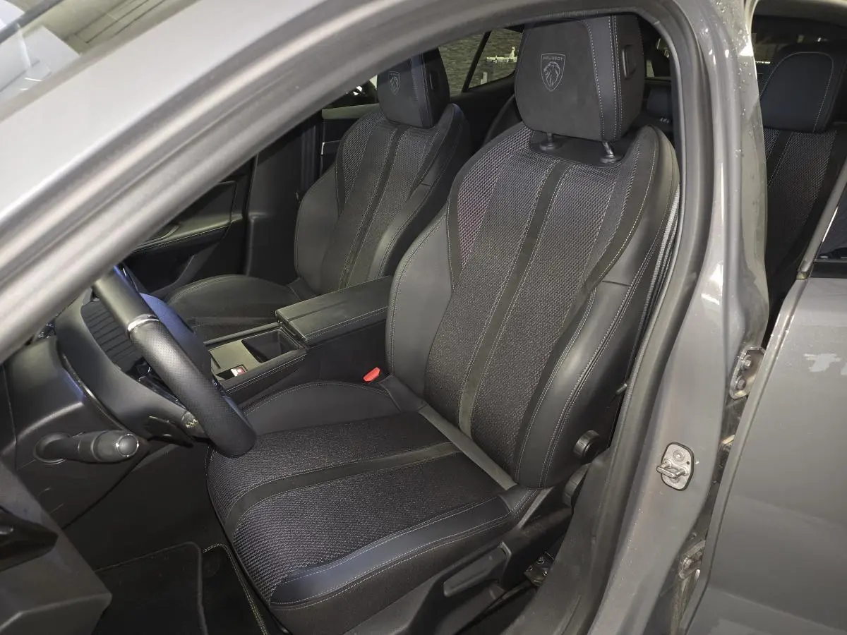 Vue intérieure côté conducteur de la Peugeot 408 gris, sièges tri-matières avec logo Peugeot brodé sur appuie-tête.