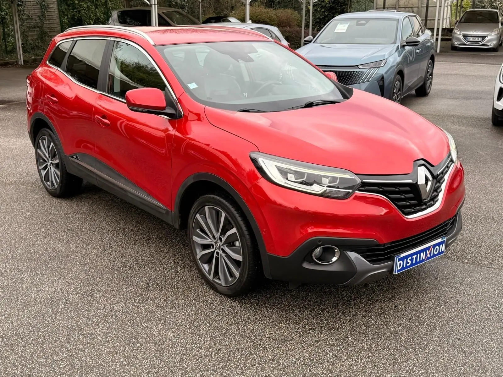 Renault Kadjar rouge flamme en 3/4 avant droit, avec calandre noire et jantes alliage bicolores visibles.