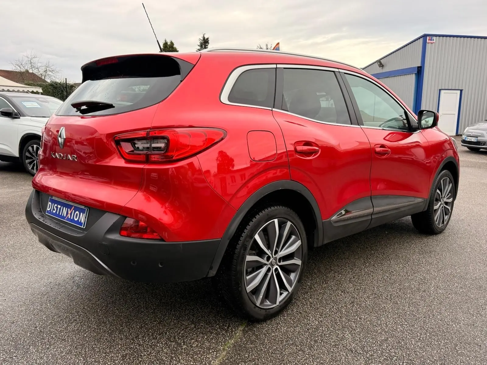 Vue 3/4 arrière droite d'un Renault Kadjar rouge flamme avec jantes alliage bi-ton et détails noirs au bas de caisse.