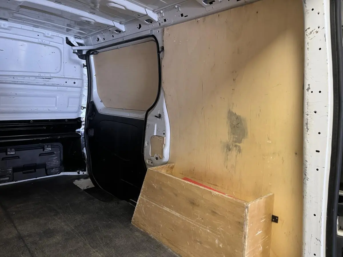 Intérieur du compartiment de chargement du Nissan Primastar blanc avec protection bois et cloison tôlée noire.