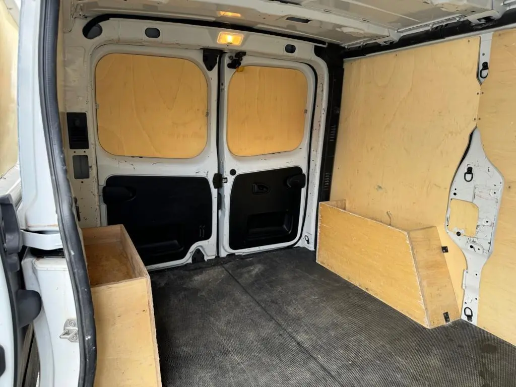 Intérieur du coffre du Nissan Primastar blanc, vue arrière avec plancher et protections latérales en bois.